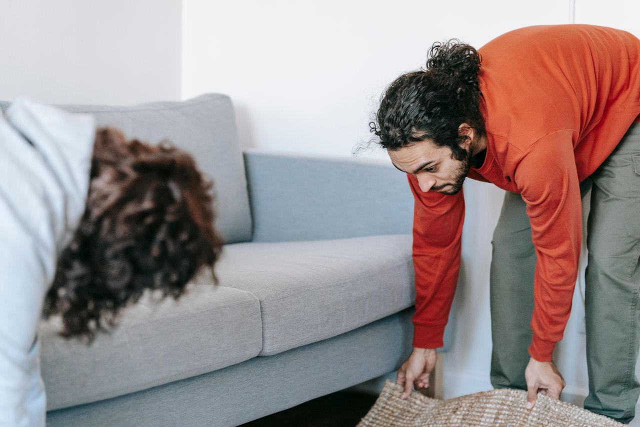 A pair of people straightening up their living room, arranging the furniture and rugs together as a team.